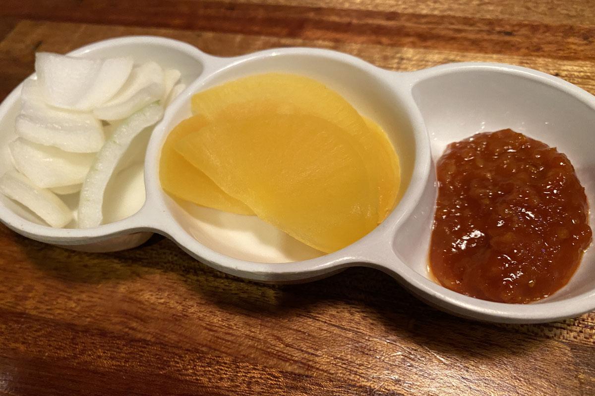 弘大飽肚烤腸的小菜，特寫黃菜頭、洋蔥及醬料的小碟子。