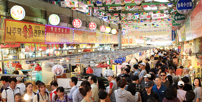 Interno affollato di un mercato tradizionale in Gwangjang, Seoul, con vari alimenti e prodotti esposti.