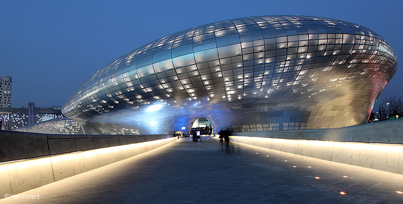 Immagine notturna del Dongdaemun Design Plaza di Seoul illuminato, mostrando architettura moderna e luci vivaci.