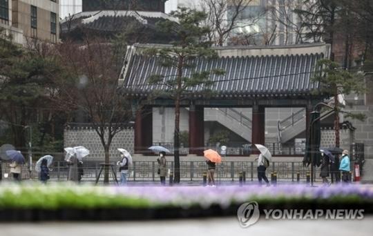 雨の中、ソウル市内で傘を差しながら並ぶ人々。「連合ニュース提供」
