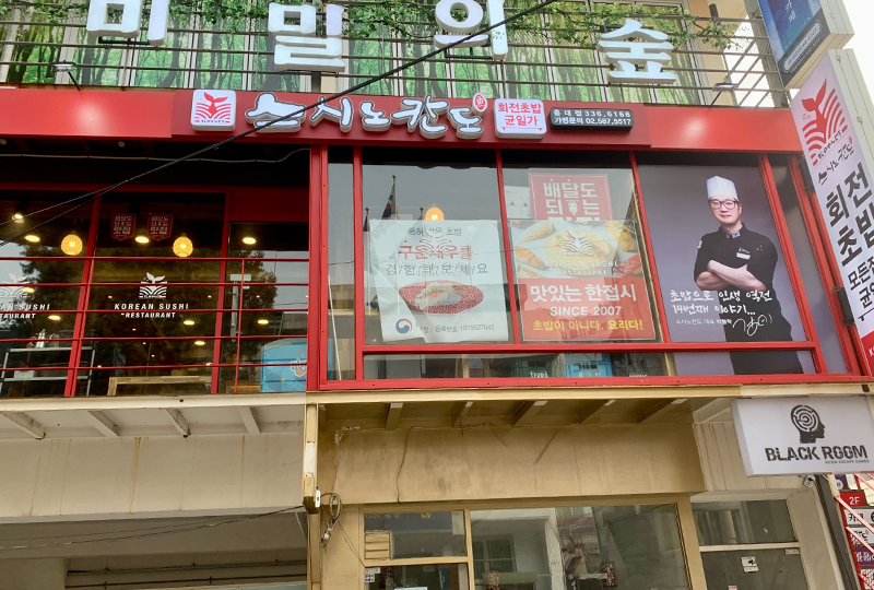 弘大的Sushi Nokando壽司店正門，展示了紅色主題的外觀和特色標誌，位於二樓。