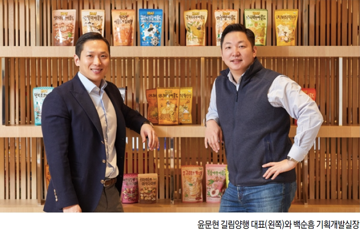 Gilim公司的代表與策劃開發室長在展示HBAF堅果產品包裝，新穎設計的包裝被陳列在他們的側後方，突顯品牌創意製作的歷程。