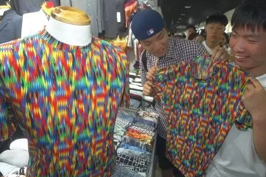 市场中展示的彩色图案T恤，旁边有顾客挑选衣物。