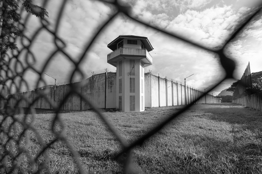 一座高墙和监狱塔楼，通过铁丝网勾勒的视角，场景如监狱环境。