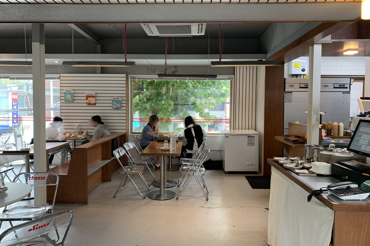 Interior del restaurante Happy Cheese Smile con mesas vacías y decoración simple en colores neutros y toques coloridos.