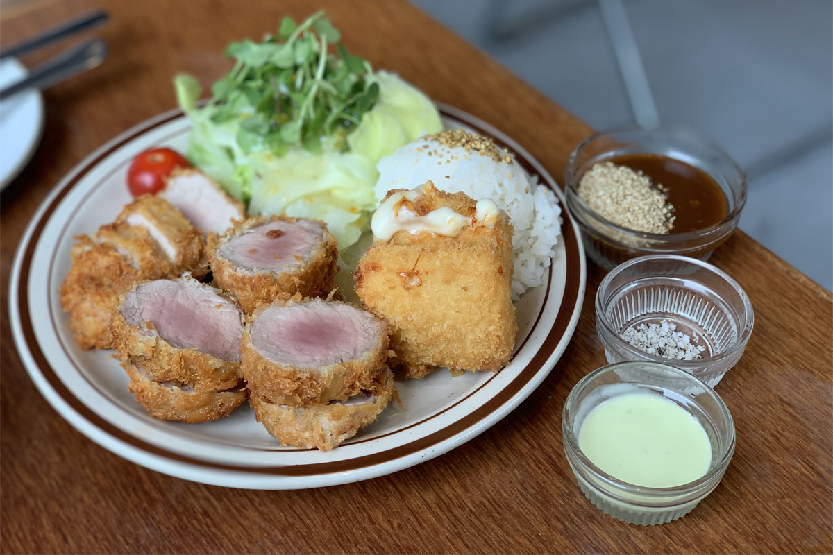 Una porción de chuleta de cerdo siendo sumergida en salsa de Happy Cheese Smile, demostrando preparación culinaria y presentación.