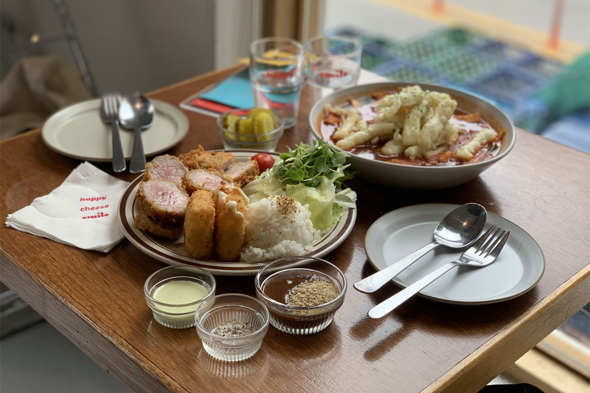 Plato de comida servida en Happy Cheese Smile, mostrando una porción generosa de tteokbokki acompañado de guarniciones y bebidas.