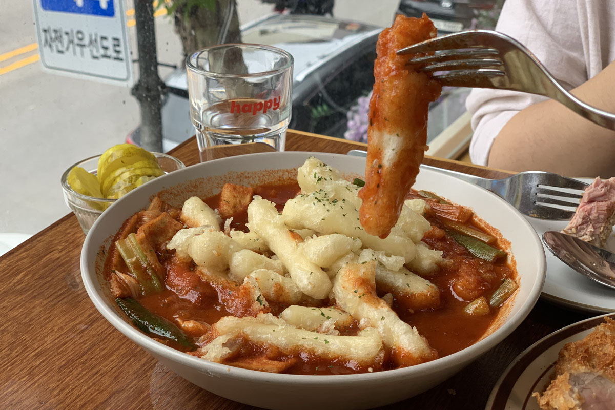 Plato de chuleta de cerdo en Happy Cheese Smile, acompañado de arroz, ensalada y pequeñas porciones de varias salsas.