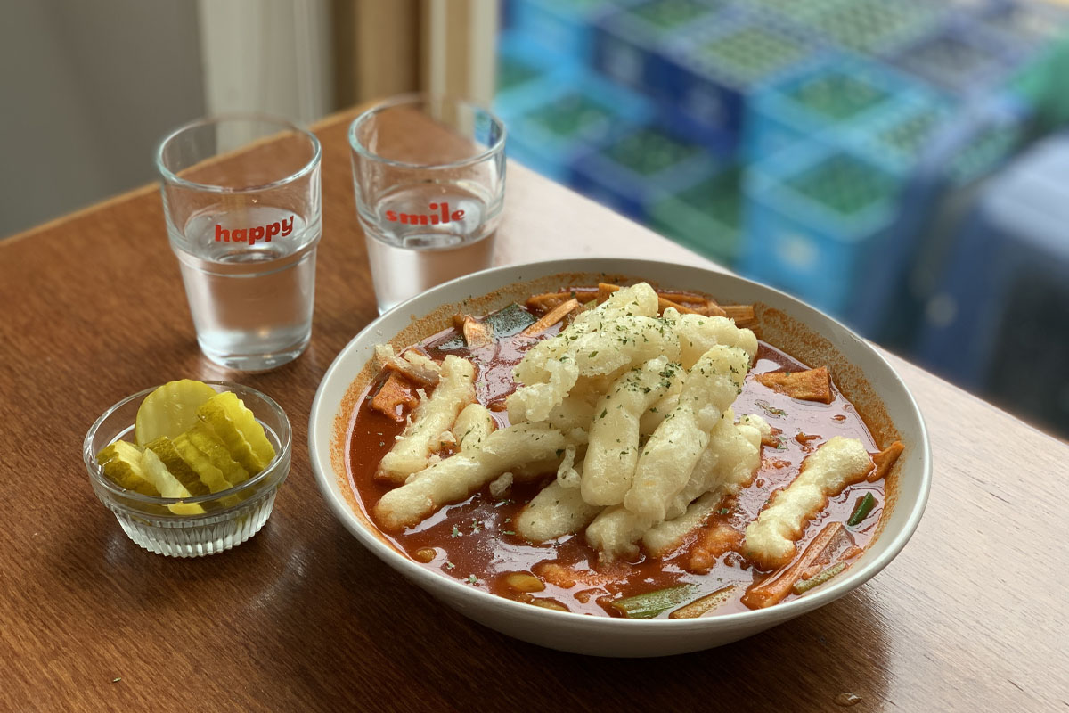 Primer plano del tteokbokki servido en Happy Cheese Smile, mostrando textura detallada con ingredientes frescos en un caldo rojo.