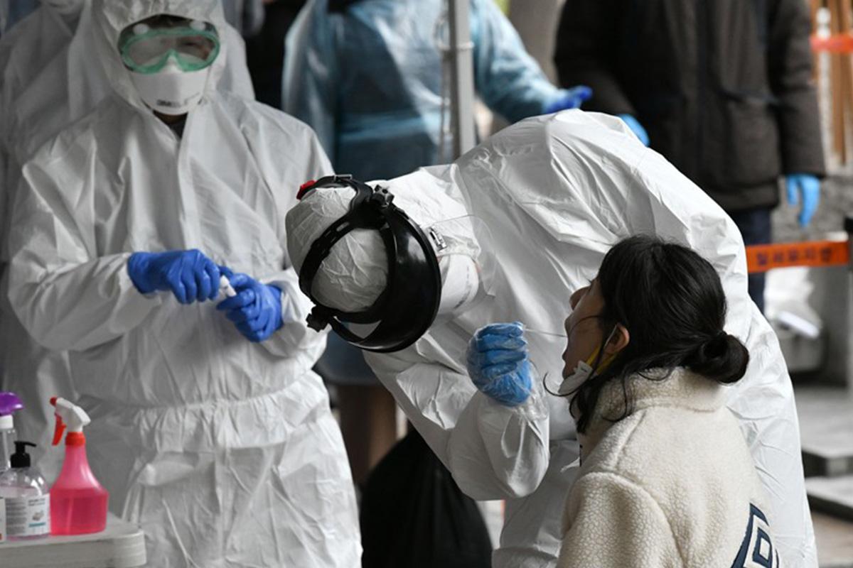 บุคลากรทางการแพทย์สวมชุดป้องกันทำการตรวจหาเชื้อ COVID-19 โดยใช้สำลีกวาดโพรงจมูกของผู้หญิงคนหนึ่ง