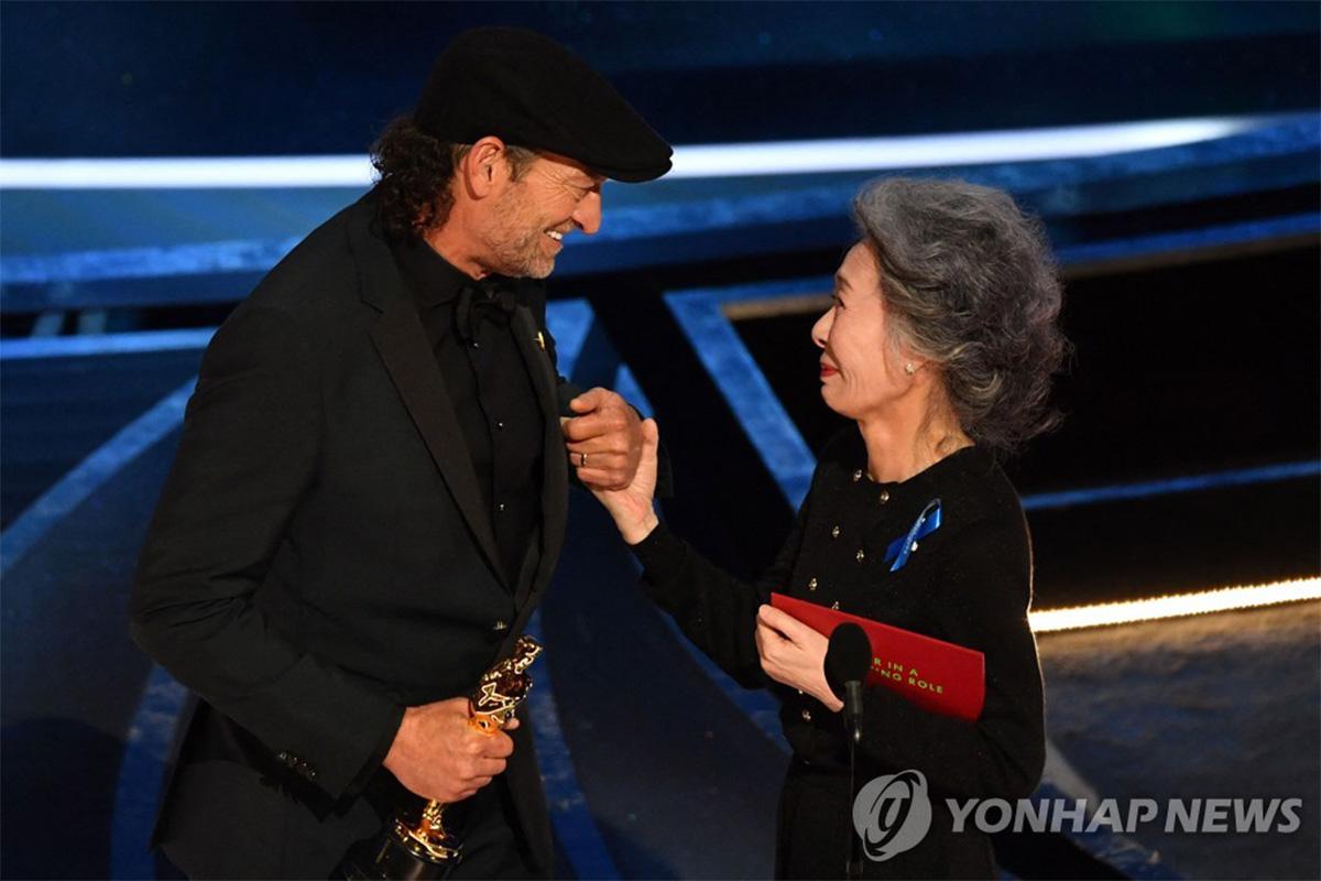 ยูน ยอจอง ยืนข้าง Troy Kotsur ในงานประกาศรางวัลออสการ์โดยมีเชิ้ตริบบิ้นสีฟ้า