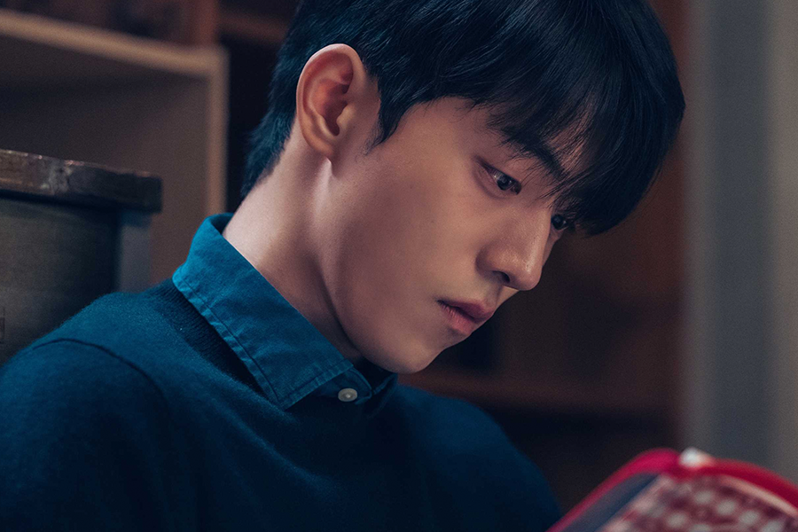 穿著深色高領毛衣的男子打開一本紅色封面的日記本，展現出閱讀時的專注與沉浸。