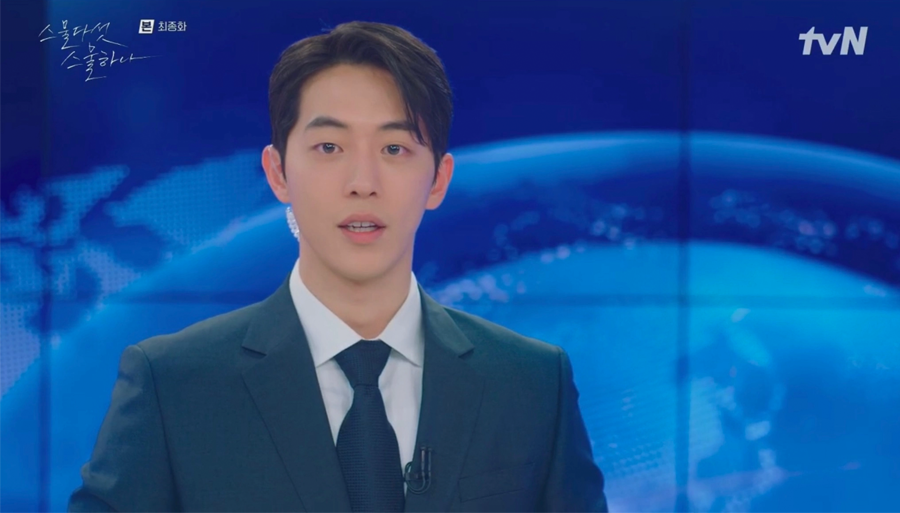戴著深色領帶的男子，背景是一個包含地球圖案的大型螢幕，顯示著新聞播報環節的專業氛圍。