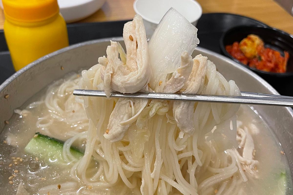 用筷子夹起的渼沙里醋鸡汤面，显示其筋道和丰富的配料。