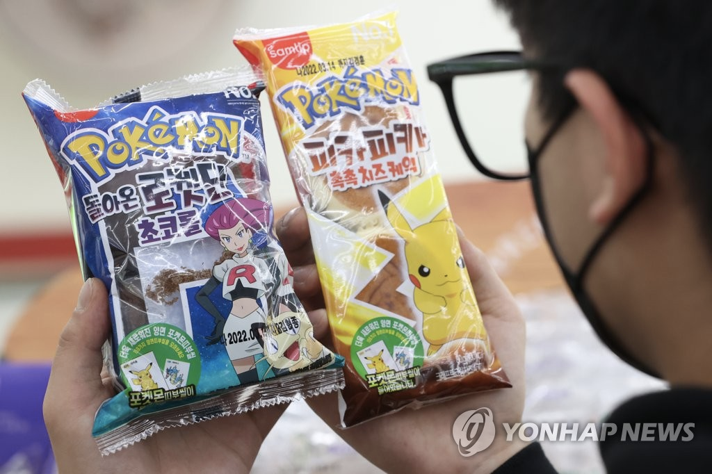 手中握有两款不同类型的宝可梦面包，包装上印有不同的宝可梦角色。