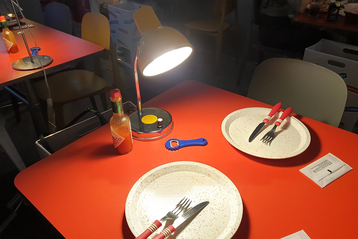 Tavolo apparecchiato all'interno di HDD Pizza con piatti e posate rosse su una superficie rossa, sotto una luce soffusa.