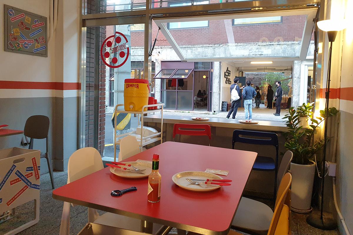 Vista dalla finestra aperta di HDD Pizza con clienti che parlano fuori, offrendo un'atmosfera rilassante e socievole.