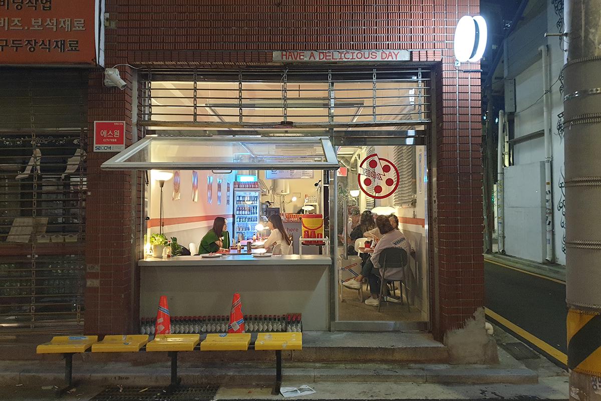 Vista esterna serale di HDD Pizza a Seongsu-dong con finestre aperte e clienti al tavolo, mostrando il suo interno accogliente e moderno.