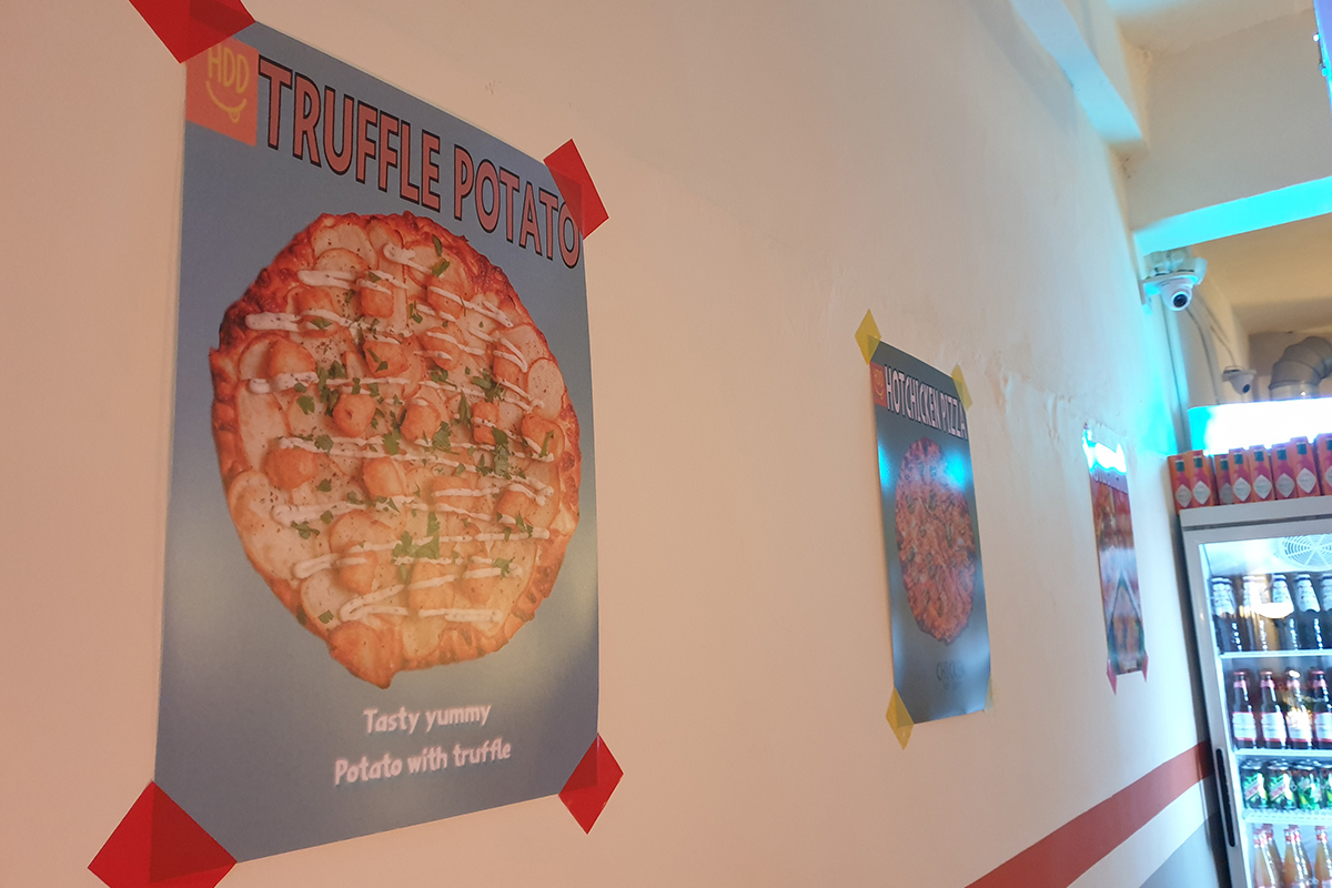 Poster decorativi di pizza al tartufo e altro all'interno di HDD Pizza, esposti su un muro bianco.