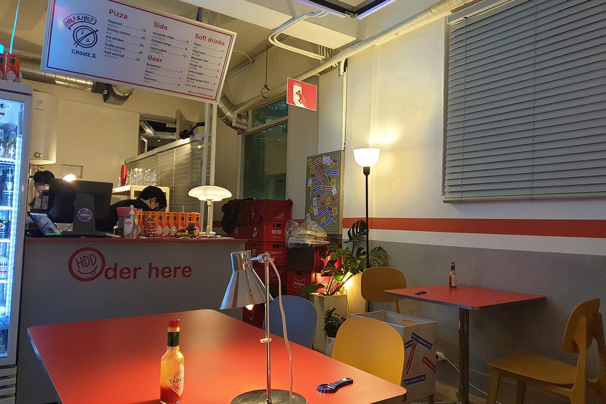 Interno di HDD Pizza con sedie colorate e tavoli rossi, creando un ambiente allegro e invitante intorno alla zona self-service.