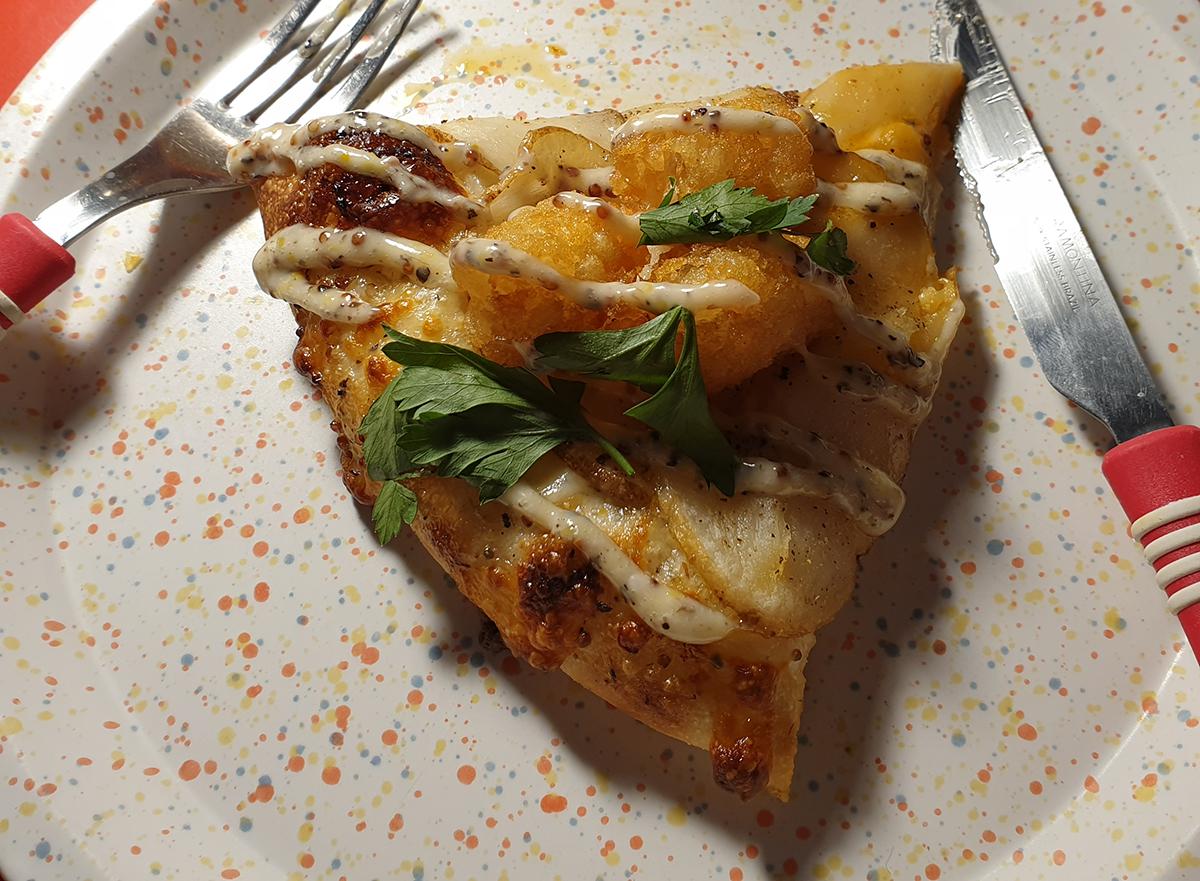 Trancio di pizza al tartufo con patate su un piatto bianco con forchetta e coltello rosso, mostrando un condimento cremoso e delizioso.