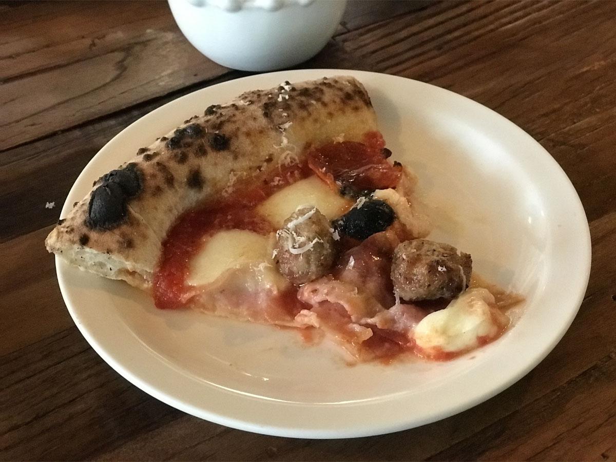 Pezzetto di pizza sottile con mozzarella e polpette su un piatto bianco.