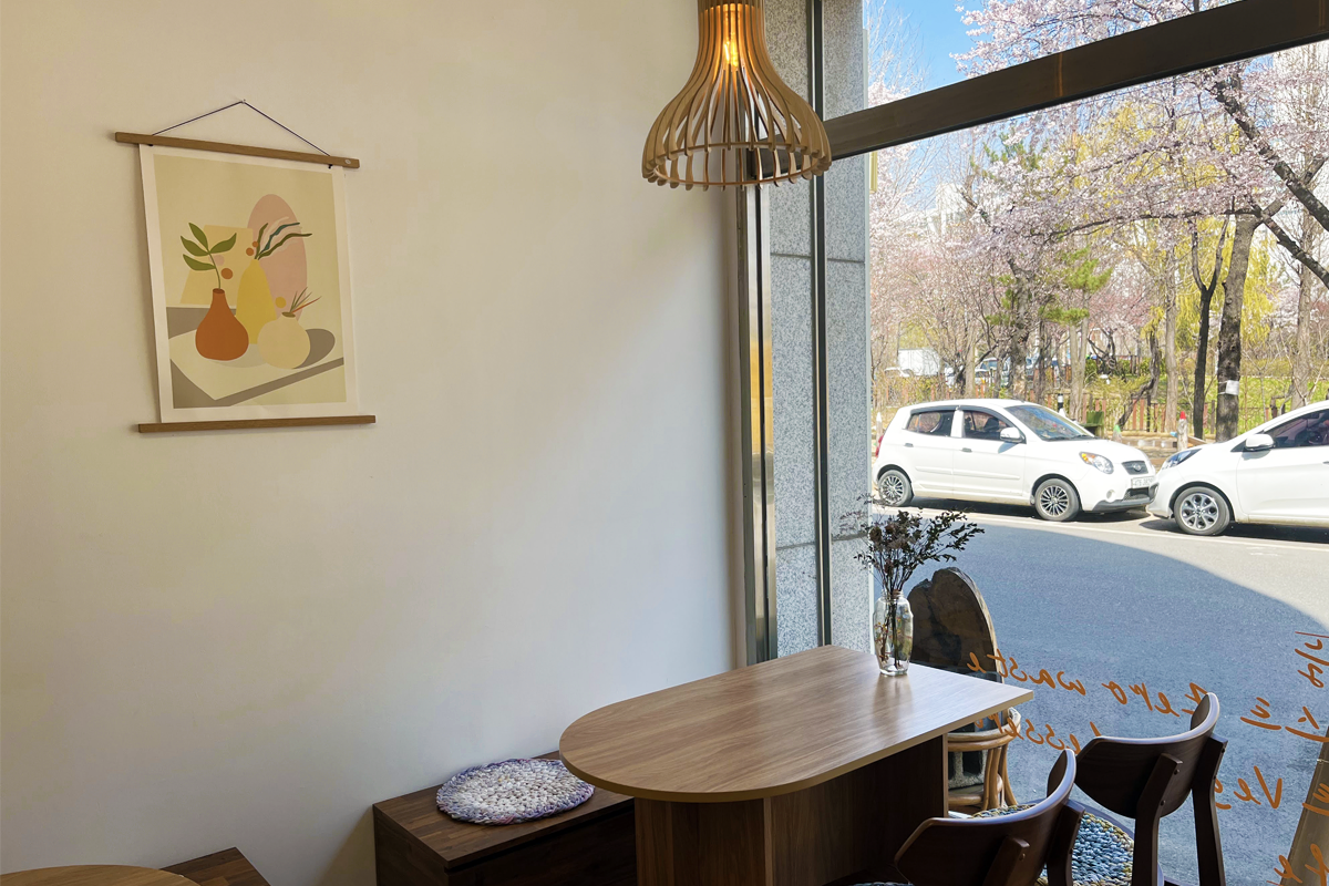 以環保概念設計的仁川素食咖啡廳內部，陽光透入窗户，暖色調氛圍，桌上擺放著乾燥花材質感的裝飾品。