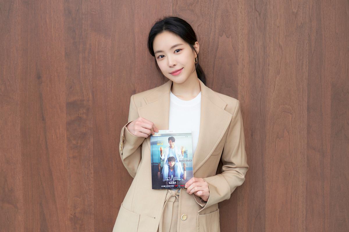 ピンク色の背景に似た画像に写る女性が手に何かを持っている