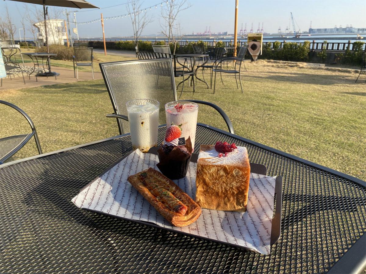 Table extérieure au soleil avec boissons et pâtisseries du café Caisson 24 avec vue sur la mer.