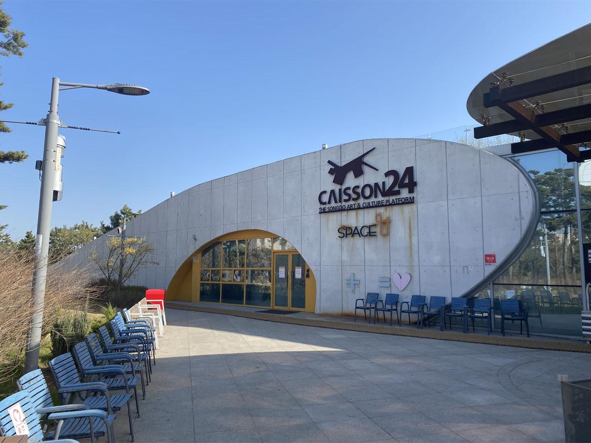 Vue extérieure de l'entrée principale du Caisson 24 à Incheon, un centre culturel avec des sièges devant.