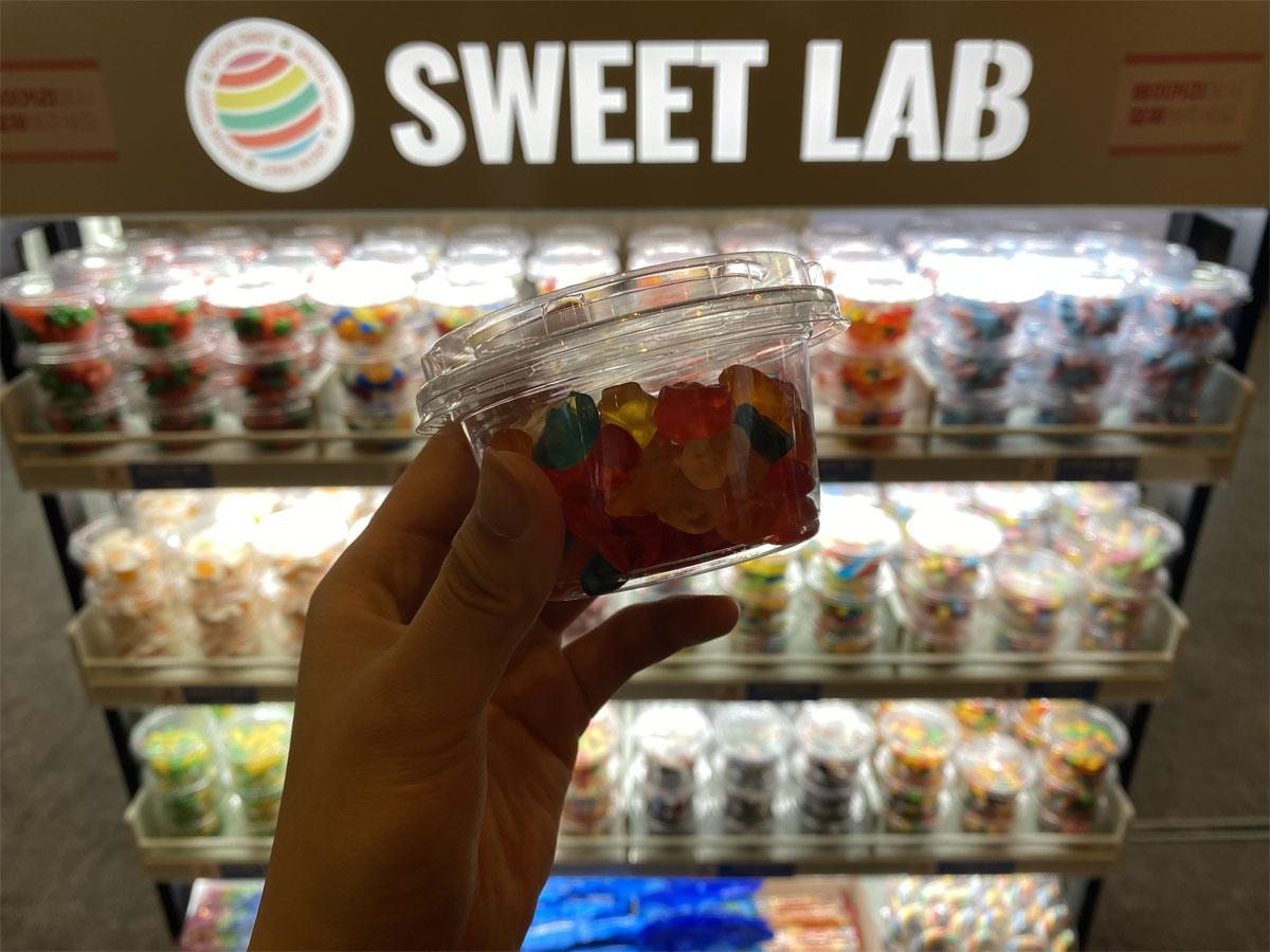 Main tenant un pot de bonbons colorés devant le coin confiseries du café Sweet Lab.