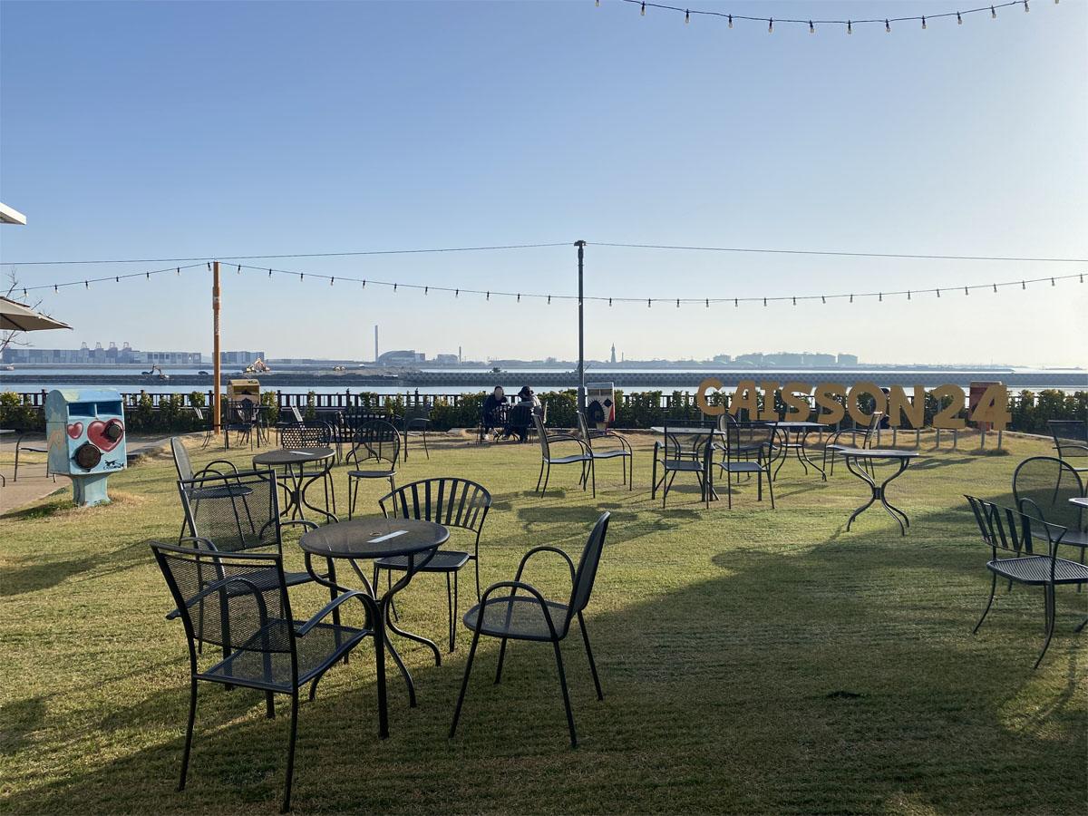 Espace extérieur du café Caisson 24 avec des tables et chaises noires et vue sur l'océan.
