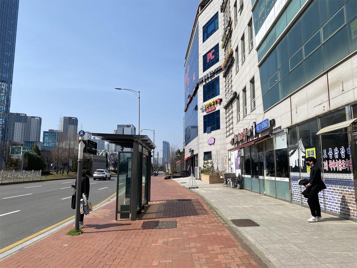 Arrêt de bus avec un abri à côté d'une vaste rue bordée de bâtiments à Incheon.