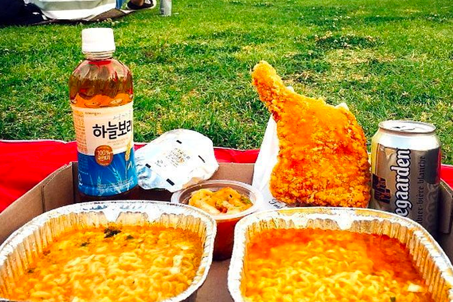 A picnic spread featuring instant ramen and drinks, set against a beautifully folded picnic blanket.