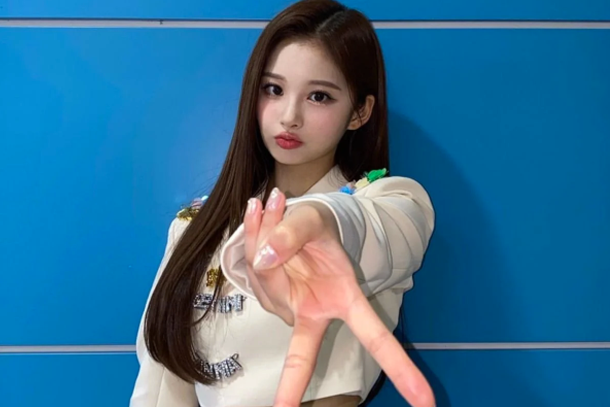 穿白色上衣的女性站在蓝色墙壁前,伸出手展示Gyaru Peace的动作,手臂和手指成为视觉焦点。