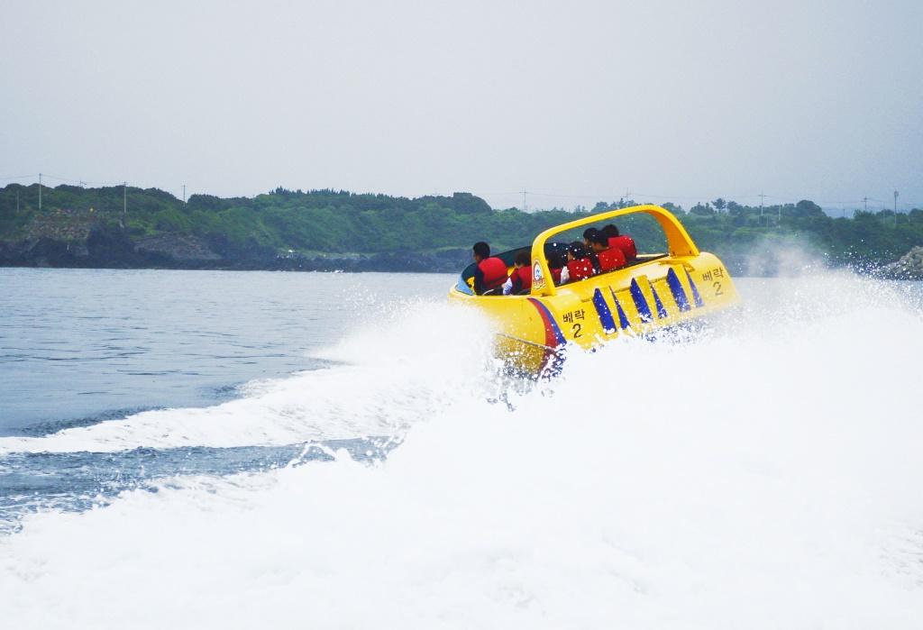 Ein Soesokkak-Jetboot flitzt mit hoher Geschwindigkeit über das blaue Wasser von Jeju Island, sprühend weiße Wellen.
