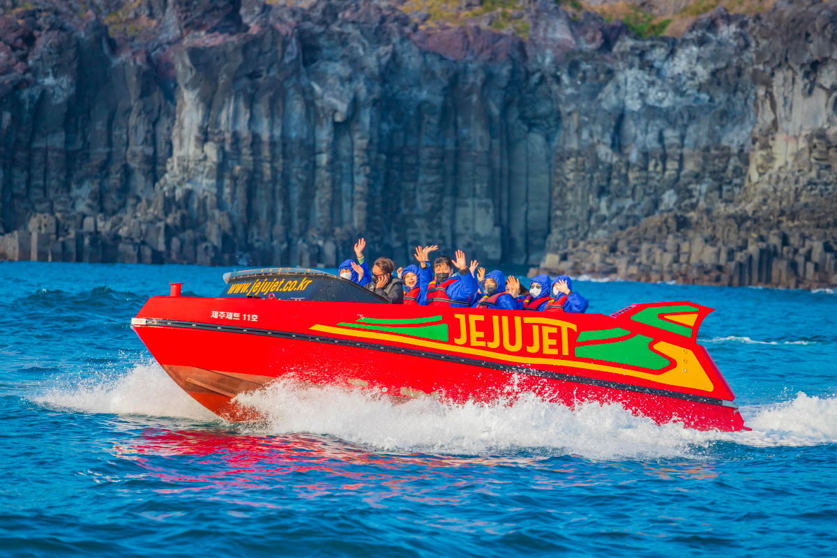 Hành khách trên thuyền phản lực Jeju Jet với vách đá Jusangjeolli hùng vĩ phía sau, đảo Jeju, Hàn Quốc
