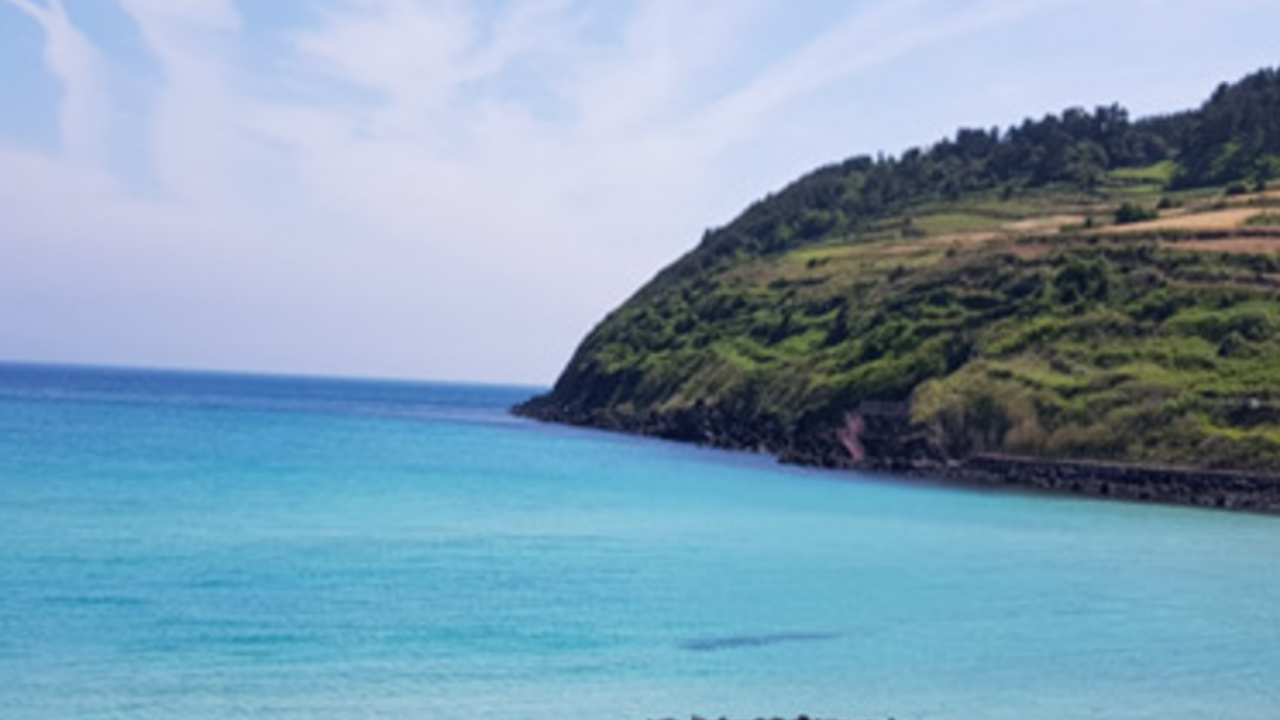 Jeju Island Küste mit türkisem Meer und grüner Hügelkulisse, bekannt für seine atemberaubende natürliche Schönheit.