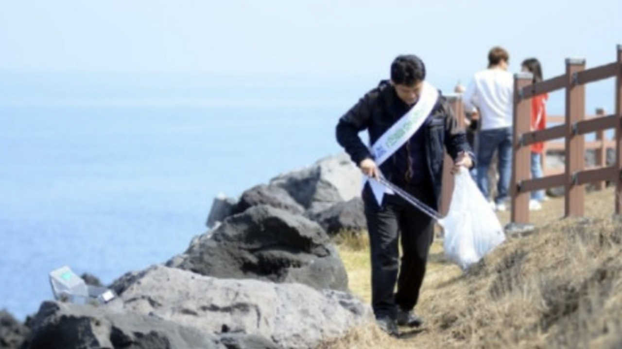 Person beim Aufsammeln von Müll an der Küste von Jeju, Teil einer umweltfreundlichen Initiative.