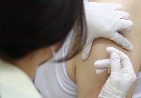 ワクチン接種を受けている人の肩に注射針が刺されている様子。医療従事者がグローブを着用して接種を行っている場面。