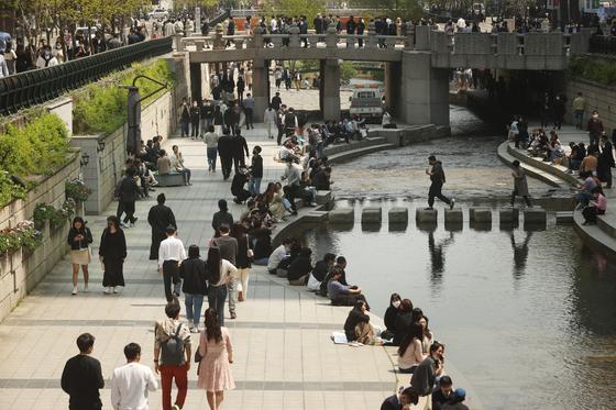 ソウルの人気観光地、清渓川で多くの人々が集まり、リラックスしている様子。暖かい天気の中で人々が散歩し、座っている風景。