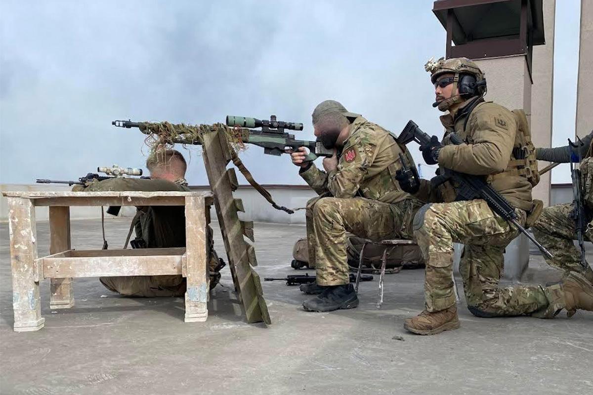 ทหารสามคนในชุดลายพรางถือปืนและกำลังปฏิบัติภารกิจบนดาดฟ้าอาคารสูง