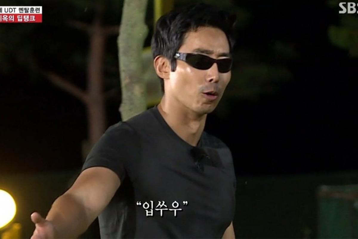 ชายในเสื้อยืดสีดำยืนอยู่กลางแจ้งพร้อมคำศัพท์เกาหลีปรากฏบนหน้าจอ