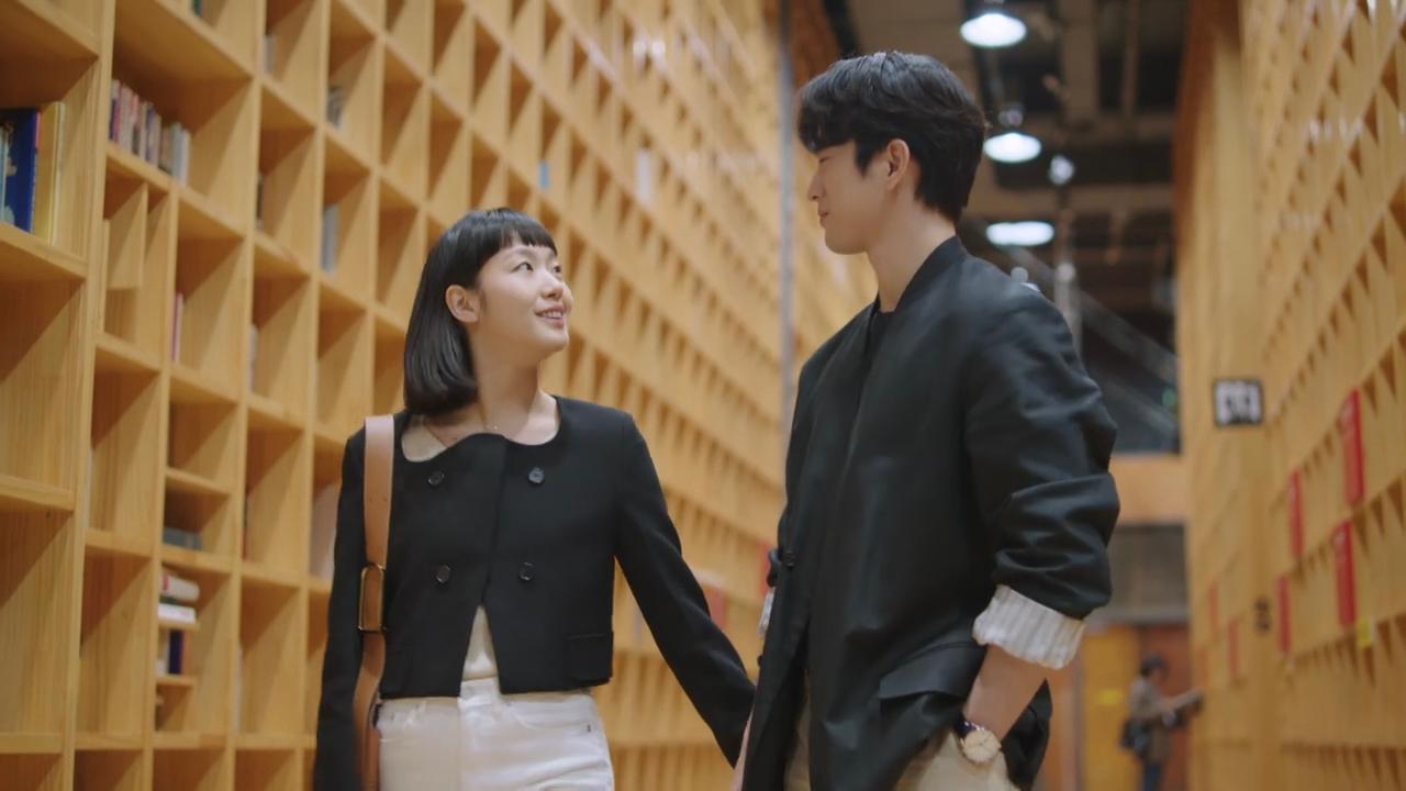 智慧之林图书馆内部,一对情侣在高大的书墙前手拉手漫步,充满文化气息的约会场所。