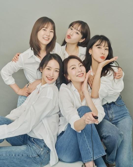 KARAメンバー5人が白いシャツとジーンズを着て、親密に寄り添って座っている団体写真