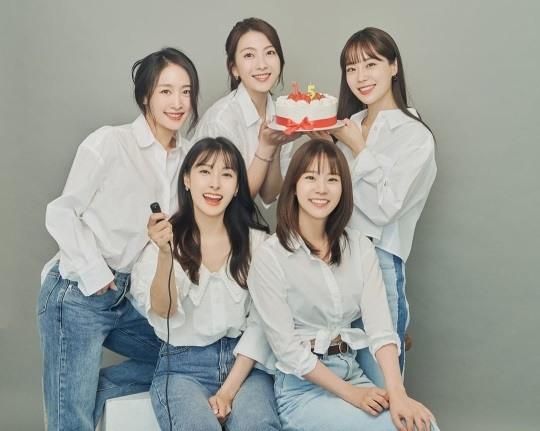 KARAメンバー5人が白いシャツとジーンズを着て、15週年のケーキを持っている団体写真