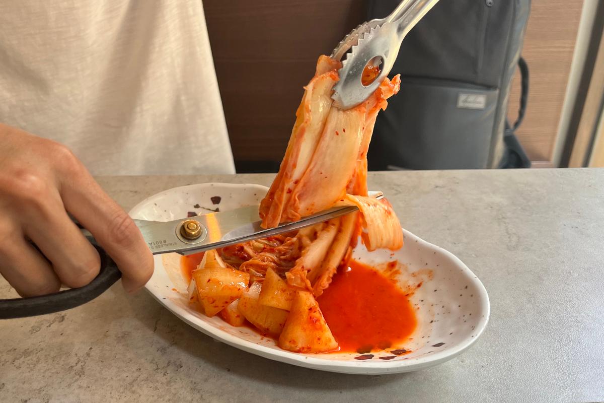 Aufschneiden des Kimchis mit einer Schere zur Kombination mit der Seolleongtang Suppe