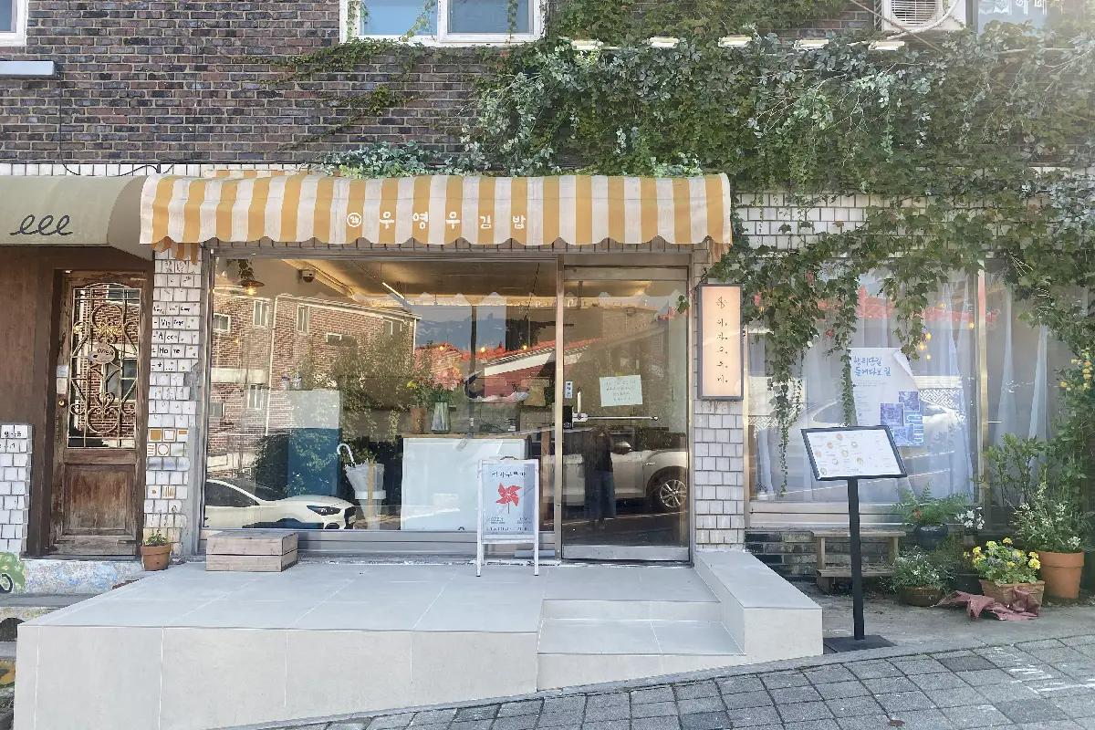 ENAドラマのロケ地『ウ・ヨンウ弁護士は天才肌』で、お父さんが運営するウ・ヨンウキムパが撮影された日本食レストラン「かざぐるま」外観。石造りの建物に、ウ・ヨンウキムパと書かれた黄色の駐車場が見える。