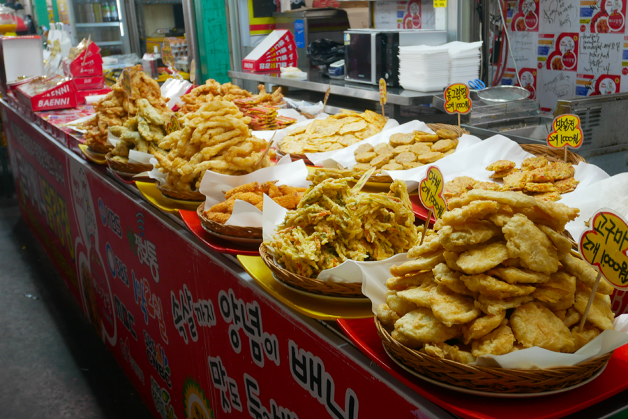 韓國江陵中央市場內的攤位，展示各式各樣的煎炸食品，豐盛的韓國小吃，吸引顧客駐足品嚐。