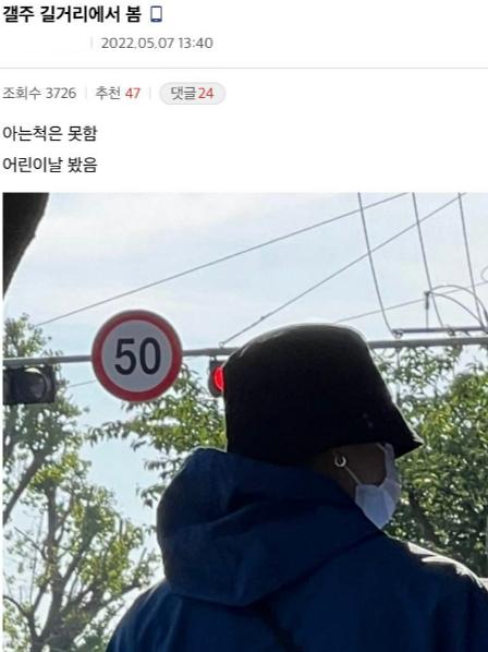 カン・スンユンが黒い帽子とマスクを着用し、青いジャケットを着て道を歩く姿の写真。背景には50キロの速度制限を示す道路標識がある。